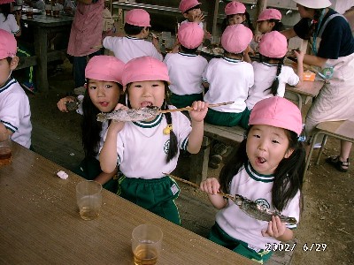 写真:串打ちしたマスの塩焼きをかぶりつく女の子たち