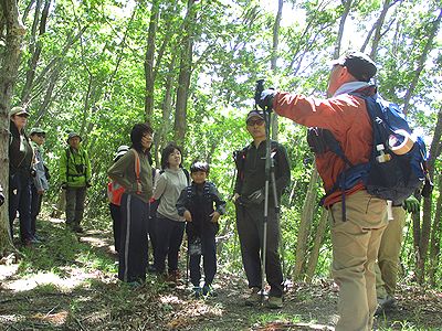 写真:新緑のやわらかい日差しの山道をでレンジャーの説明を聞く参加者たち
