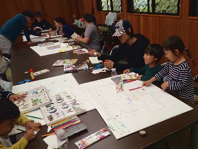 写真:机に大きいマップを広げて、図鑑を見ながら真剣に取り組む親子